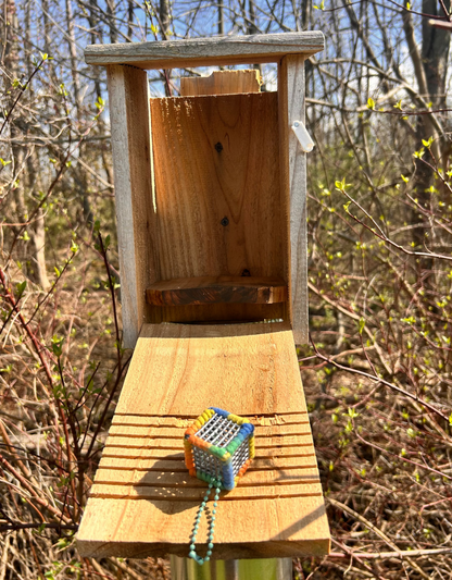 Handmade ASMR sensory cube laced with cotton multicolored yarn, 1.25 in. hexagon fidget art with a light green ball chain clip pictured in a wooden bird watch box tower.