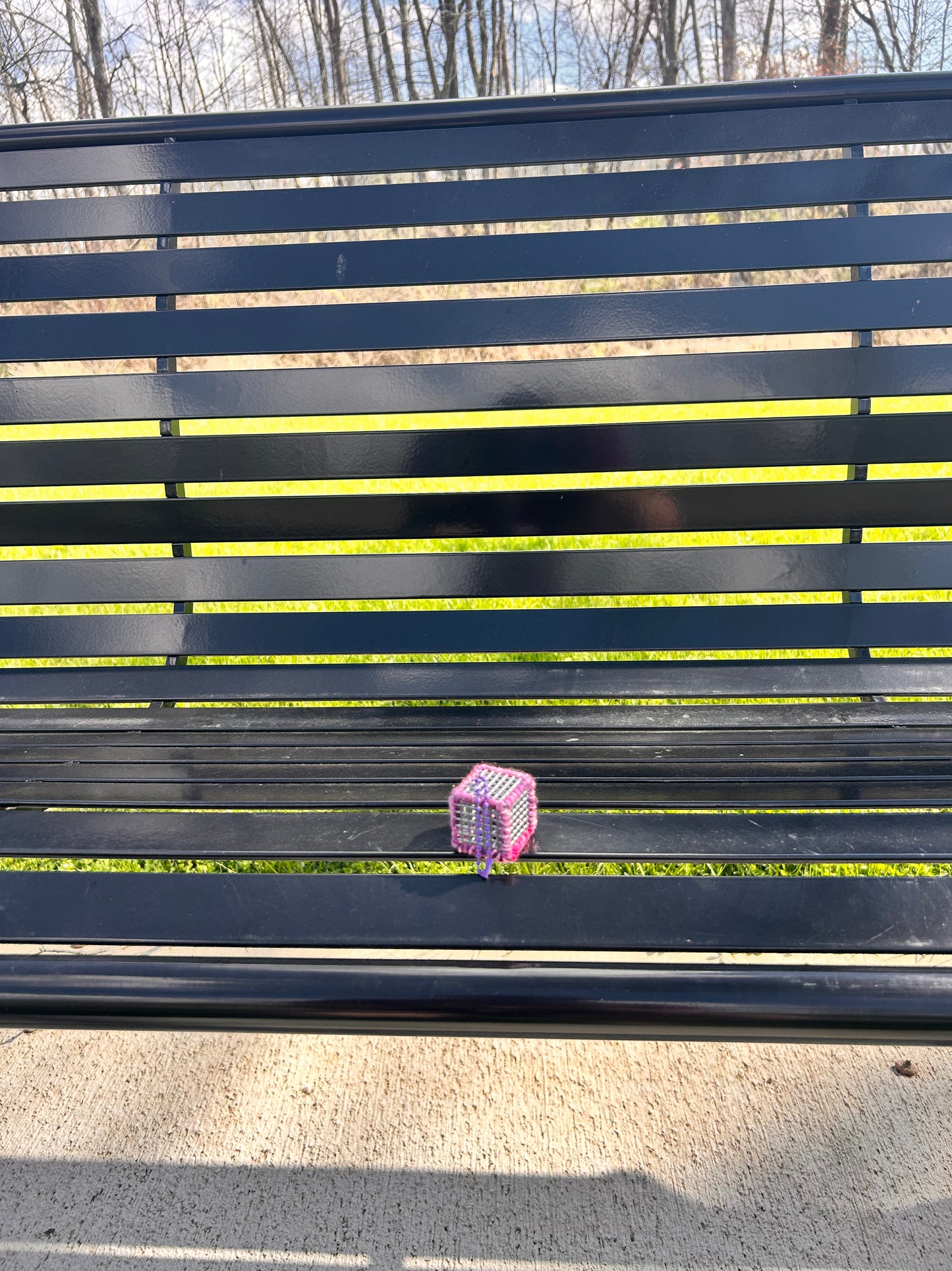 Handmade Pink and purple yarn laced Flex-Hex-Sensi © key chain - AMSR / Sensory cube with a purple ball chain sitting on a black metal bench in the sun with grass and trees in the background.